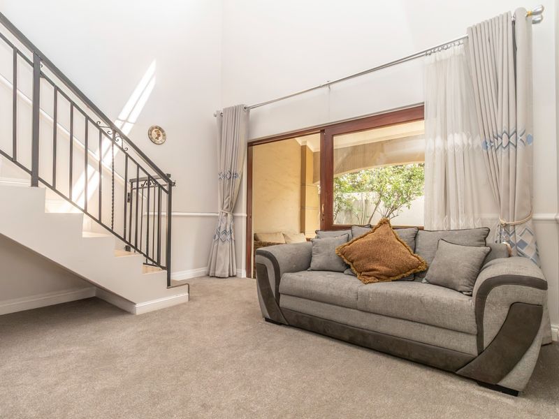 A bright living room featuring high ceilings, a wrought iron staircase, and a sliding glass door providing access to the outdoor patio area.