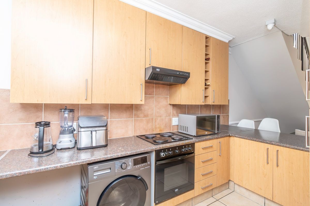 Functional kitchen featuring light wood-finish cabinetry, laminate countertops, tiled backsplash, and integrated cooking appliances, offering a practical layout for daily use.