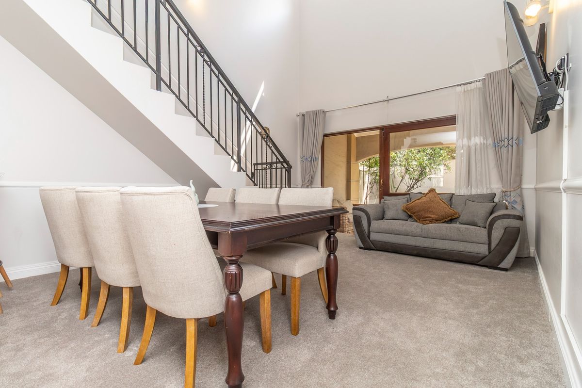 Spacious living and dining area featuring high ceilings, a staircase with wrought iron balustrade, and sliding glass doors leading to the patio.