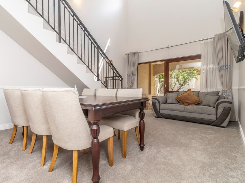Spacious living and dining area featuring high ceilings, a staircase with wrought iron balustrade, and sliding glass doors leading to the patio.