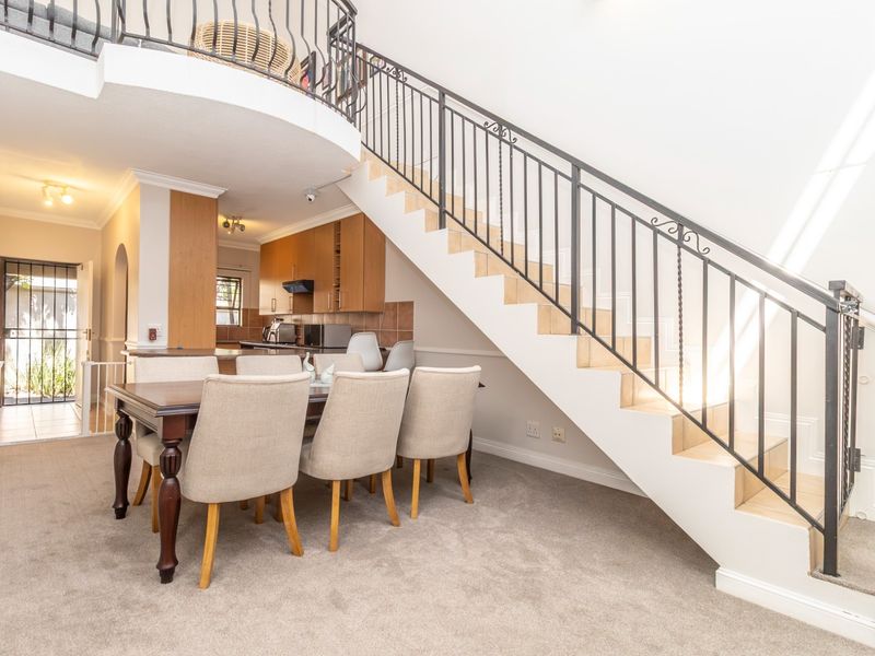 Open plan living and dining area featuring a staircase with wrought iron balustrade, leading to a functional kitchen with built-in cabinetry.