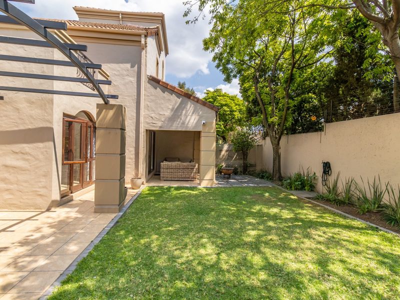 A well-maintained rear garden featuring a tiled patio area with a pergola, a neat lawn, and secure boundary walls.