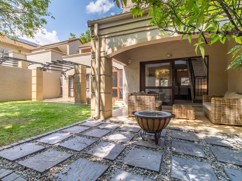 A well-maintained rear exterior featuring a covered patio with tiled flooring, stone pavers, and a landscaped lawn area.