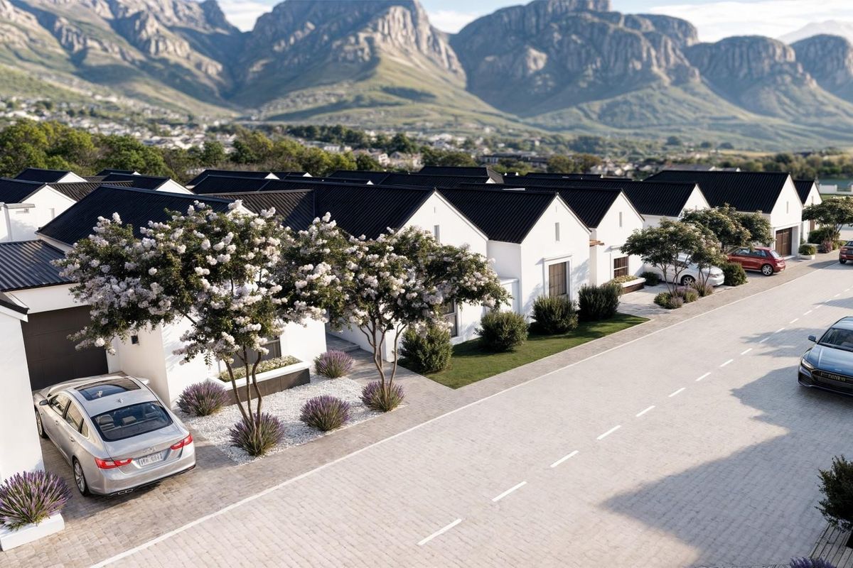 An aerial view of a modern residential estate featuring uniform white houses with dark pitched roofs, paved driveways, and scenic mountain views.
