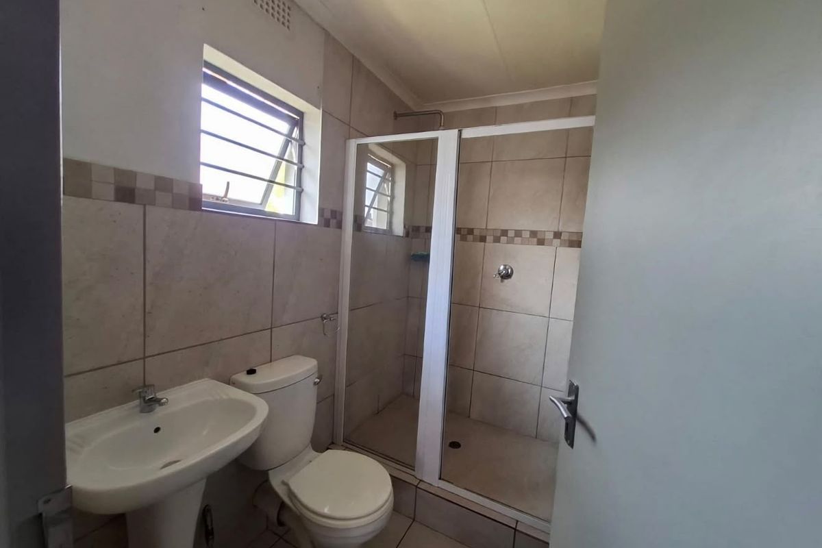 A functional bathroom featuring a pedestal basin, toilet, and a tiled shower enclosure with a louvered window for ventilation.