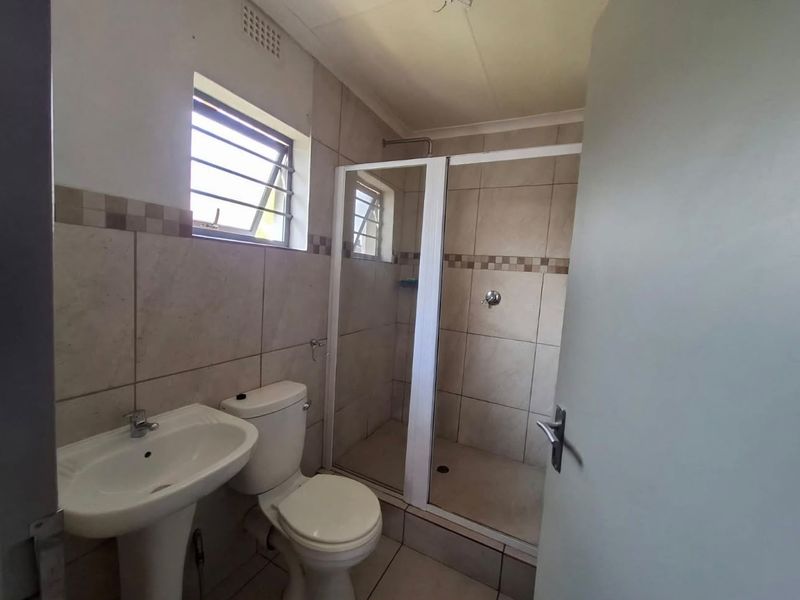 A functional bathroom featuring a pedestal basin, toilet, and a tiled shower enclosure with a louvered window for ventilation.
