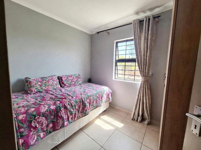 A compact bedroom featuring tiled flooring, a window with security bars, and a built-in cupboard, offering a functional and neutral living space.