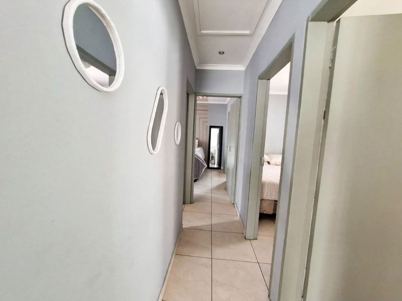 A functional hallway featuring tiled flooring and recessed downlighting, providing access to adjacent bedrooms.