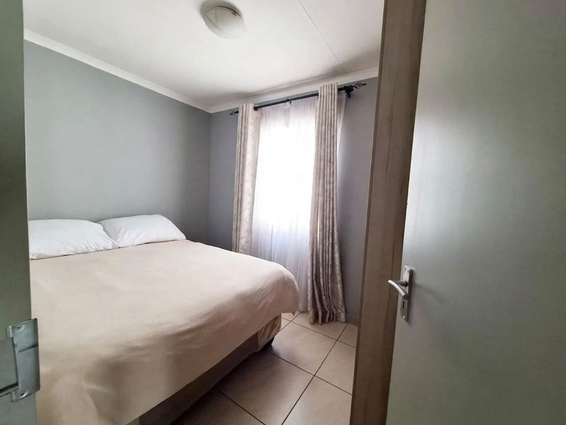 A compact bedroom featuring neutral grey walls, tiled flooring, and a window dressed with curtains.