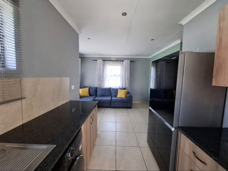Open-plan kitchen and living area featuring modern granite countertops, wood-finish cabinetry, and neutral tiled flooring throughout the space.