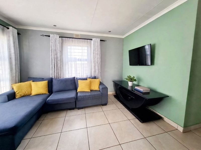 A well-maintained living room featuring neutral tiled flooring, recessed downlighting, and a feature wall, providing a comfortable and functional living space.