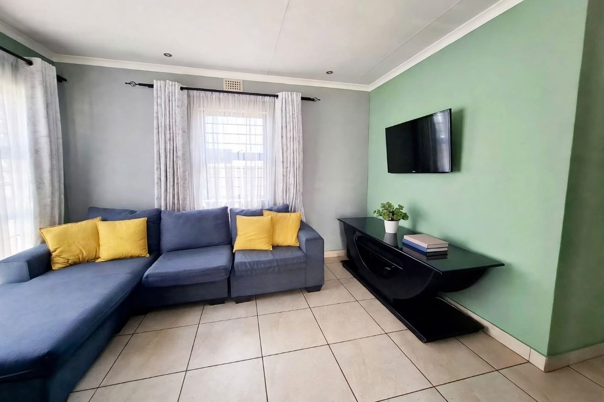 A well-maintained living room featuring neutral tiled flooring, recessed downlighting, and a feature wall, providing a comfortable and functional living space.