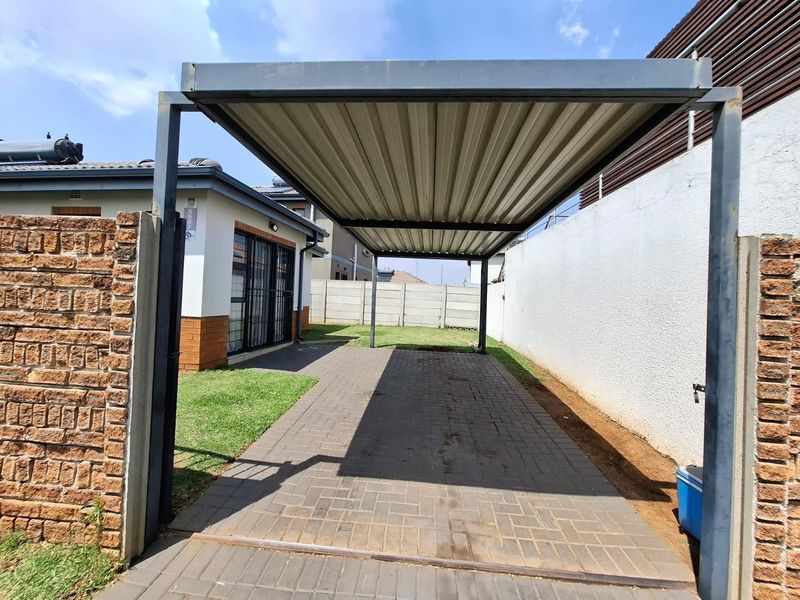 A functional outdoor carport with a paved driveway, situated alongside a residential building with brick and precast concrete boundary walls.