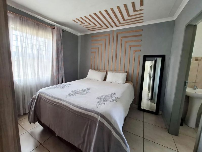 A well-maintained bedroom featuring decorative wall paneling, tiled flooring, and an en-suite area with a pedestal basin.
