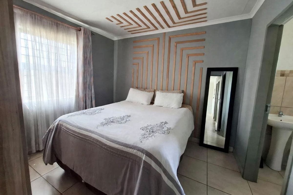 A well-maintained bedroom featuring decorative wall paneling, tiled flooring, and an en-suite area with a pedestal basin.