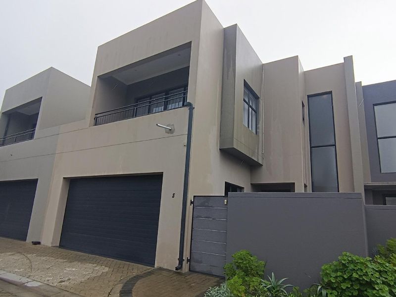 Modern double-story townhouse featuring a contemporary facade, integrated double garage, and an upper-level balcony with metal railings.