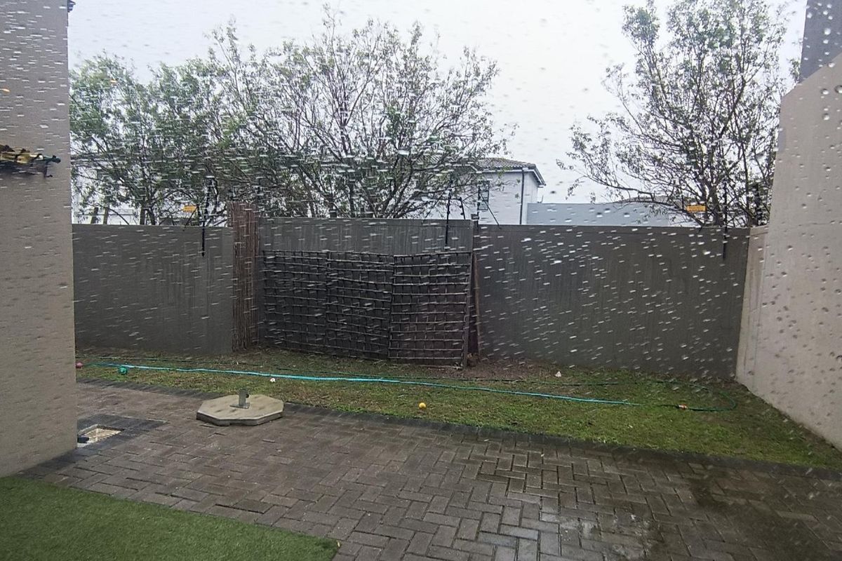 A rear exterior view of a paved patio area with boundary walls and a small section of artificial grass.