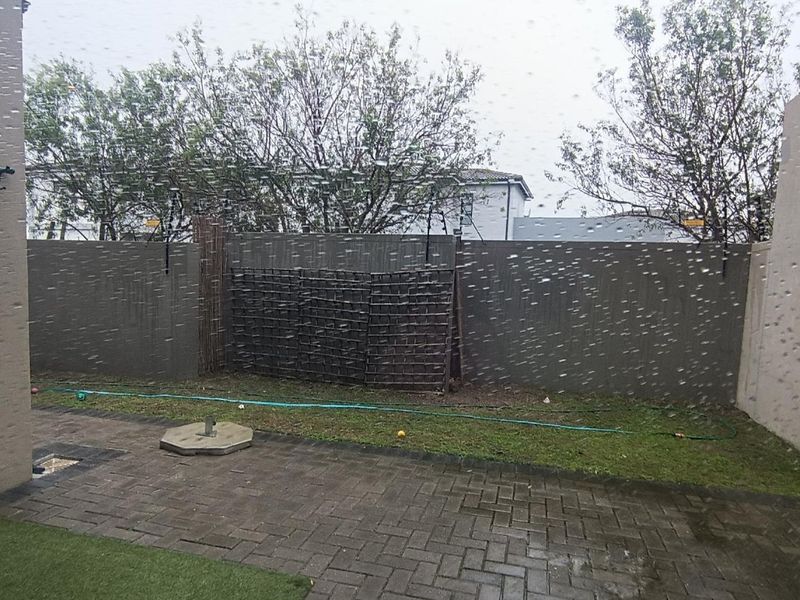 A rear exterior view of a paved patio area with boundary walls and a small section of artificial grass.