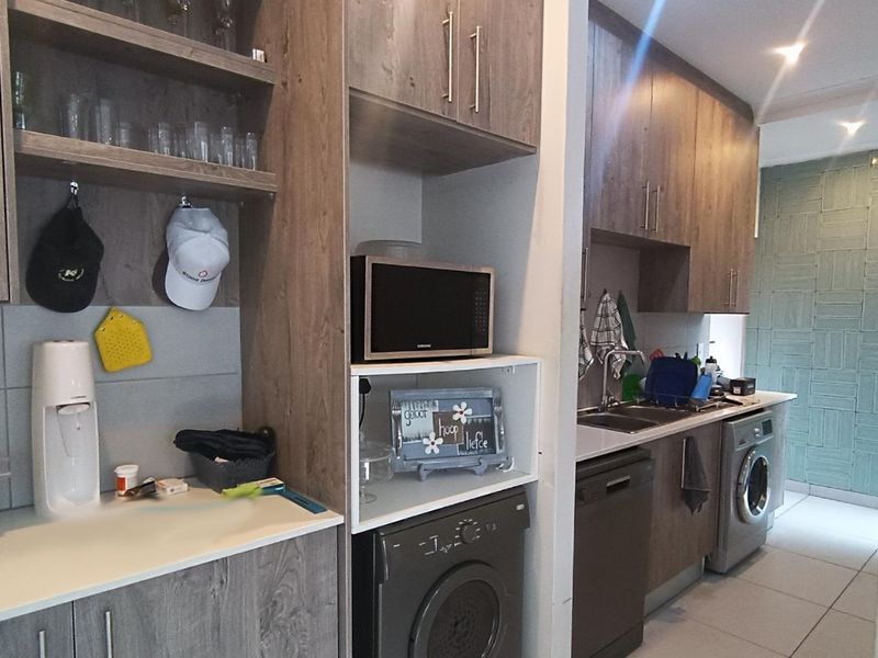 A functional scullery area featuring wood-look cabinetry, integrated appliance spaces, stainless steel sink, and tiled finishes, providing additional utility and storage space.