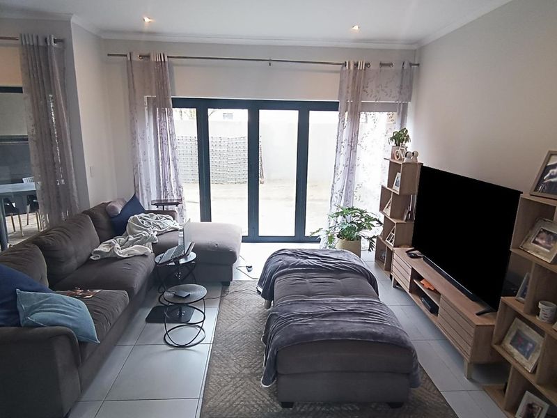 A well-lit living room featuring large aluminium sliding doors that provide access to the outdoor area and neutral tiled flooring throughout.