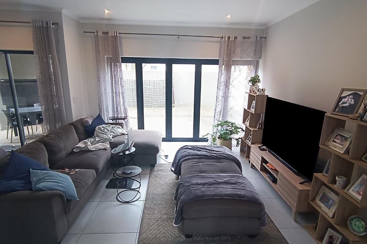 A well-lit living room featuring large aluminium sliding doors that provide access to the outdoor area and neutral tiled flooring throughout.