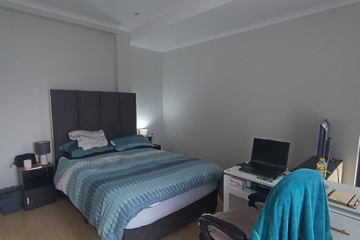 A well-lit bedroom featuring laminate flooring, a recessed ceiling, and a glass panel door providing natural light.