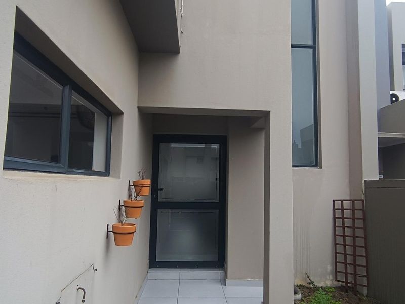 Modern entrance area featuring a frosted glass door, tiled porch, and contemporary aluminium framed windows with neutral exterior wall finishes.