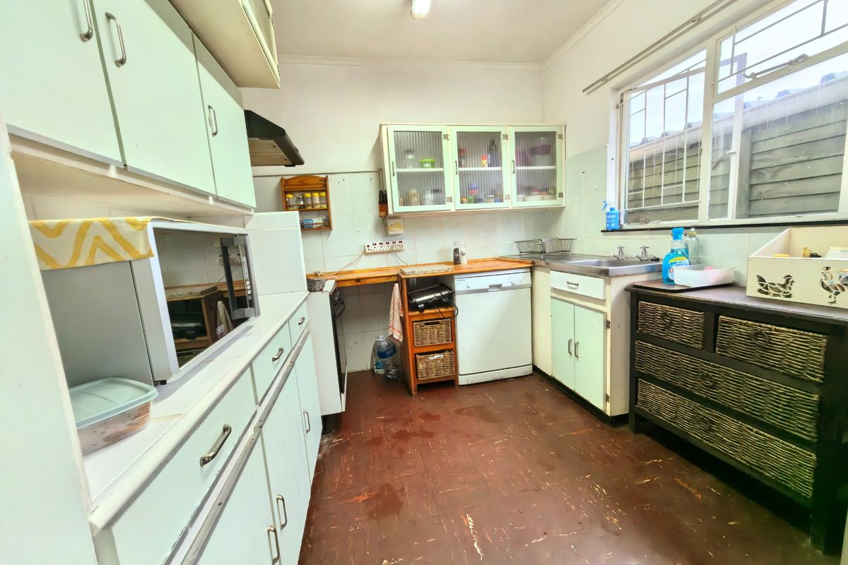 A functional kitchen featuring built-in cabinetry, a stainless steel sink, and a tiled splashback, offering potential for modernization and cosmetic updates.