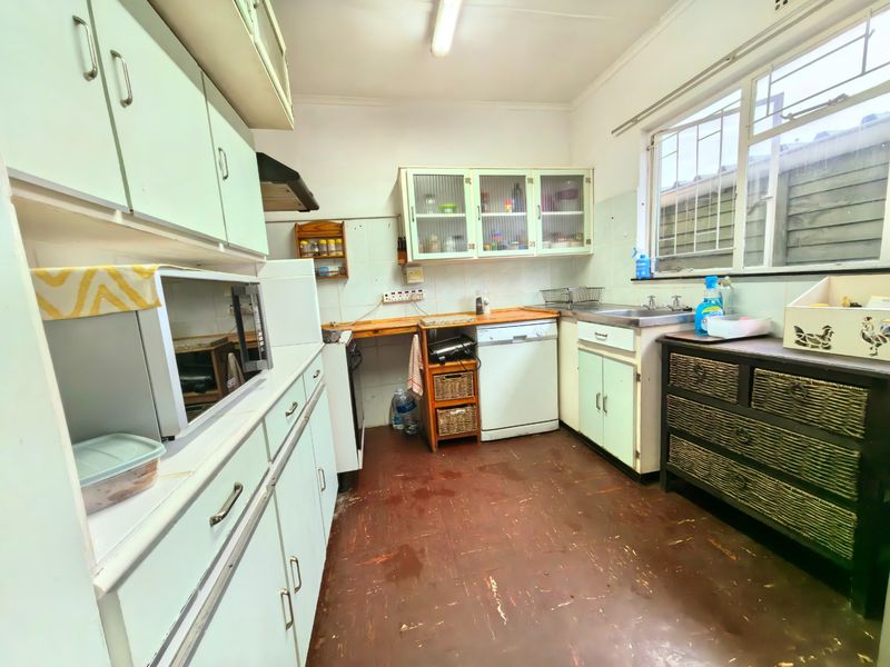 A functional kitchen featuring built-in cabinetry, a stainless steel sink, and a tiled splashback, offering potential for modernization and cosmetic updates.