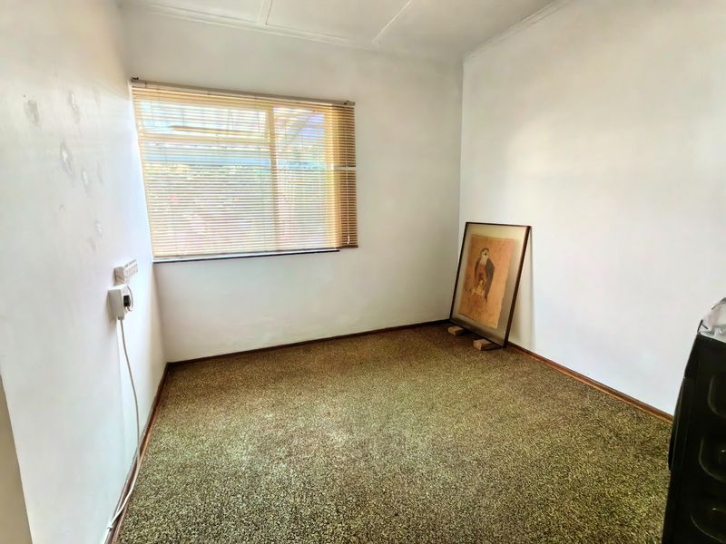 A vacant bedroom featuring carpet flooring, a window with venetian blinds, and electrical wall outlets, ready for renovation or staging.