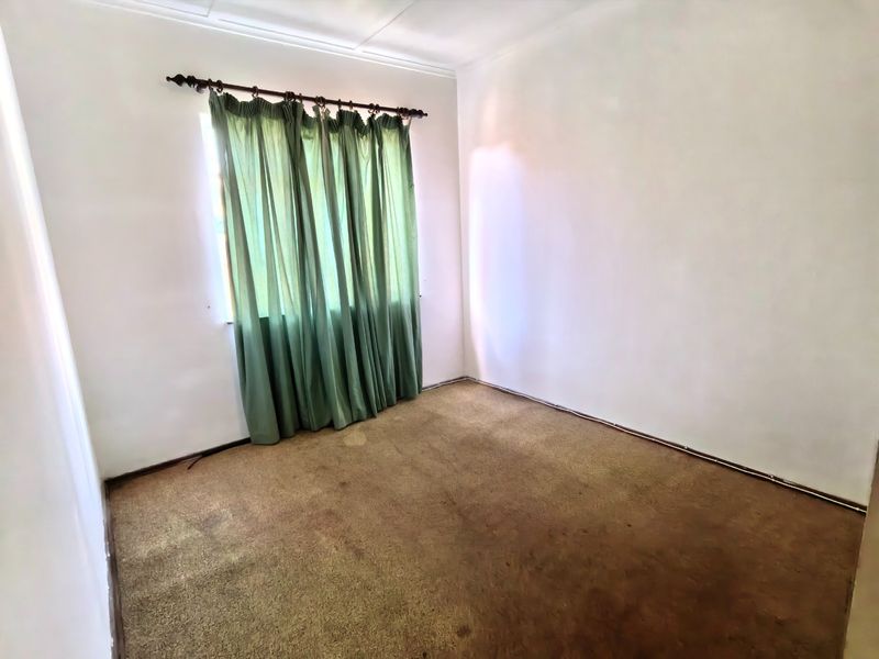An empty bedroom featuring neutral walls and worn, stained carpeting, providing a blank canvas for renovation or interior design updates.