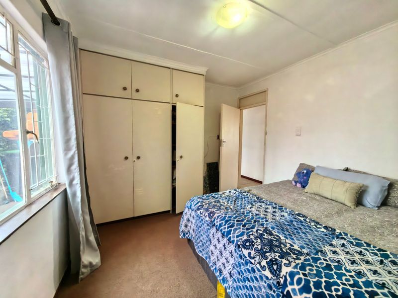 A bedroom featuring built-in cupboards, carpeted flooring, and security bars on the window, offering a functional space with potential for cosmetic updates.