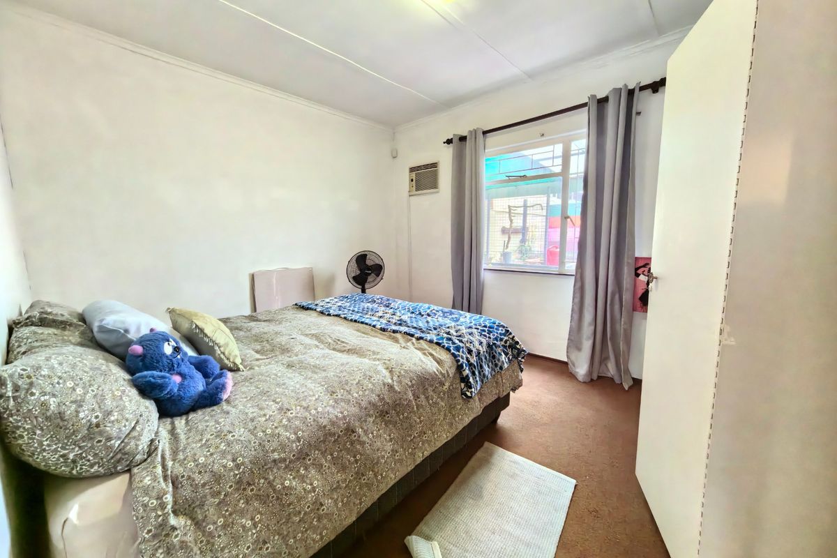 A functional bedroom featuring a window, built-in cupboard, and wall-mounted air conditioning unit.