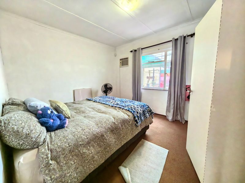 A functional bedroom featuring a window, built-in cupboard, and wall-mounted air conditioning unit.