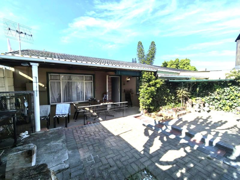A rear exterior view of the house featuring a paved patio area and a covered veranda with a tiled roof.