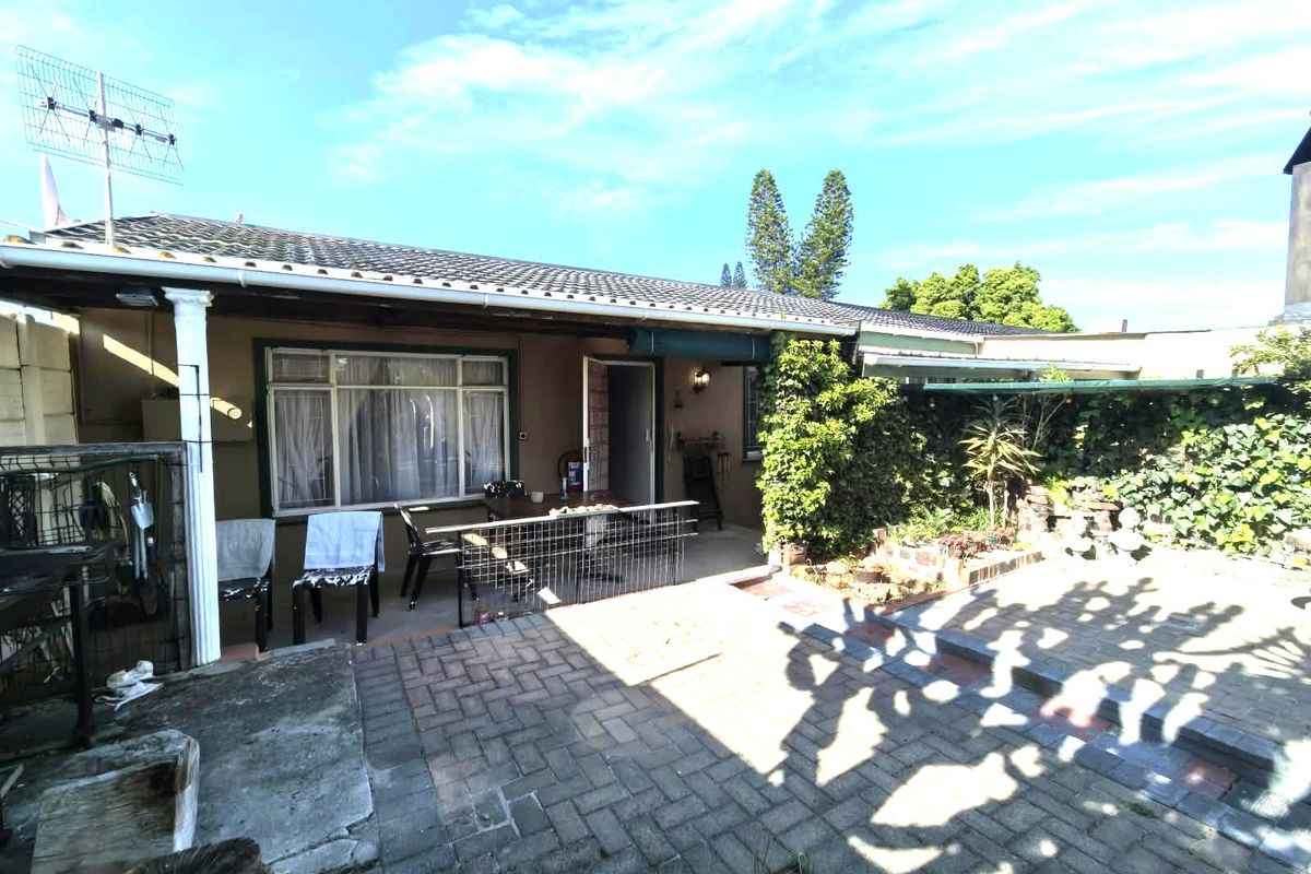A rear exterior view of the house featuring a paved patio area and a covered veranda with a tiled roof.