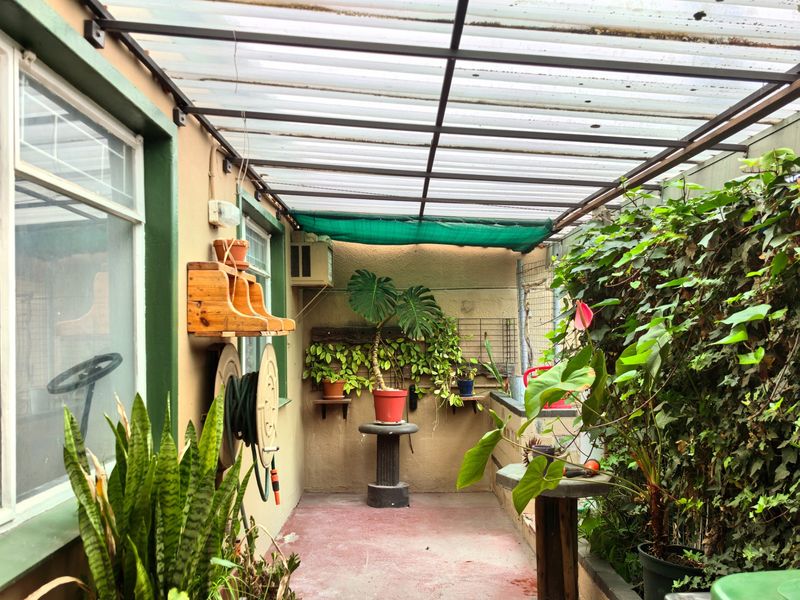 A covered patio area featuring a translucent polycarbonate roof, concrete flooring, and an external wall-mounted air conditioning unit.