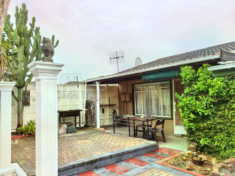 Rear exterior view featuring a paved patio area, brick retaining wall, and established garden elements adjacent to the main dwelling structure.