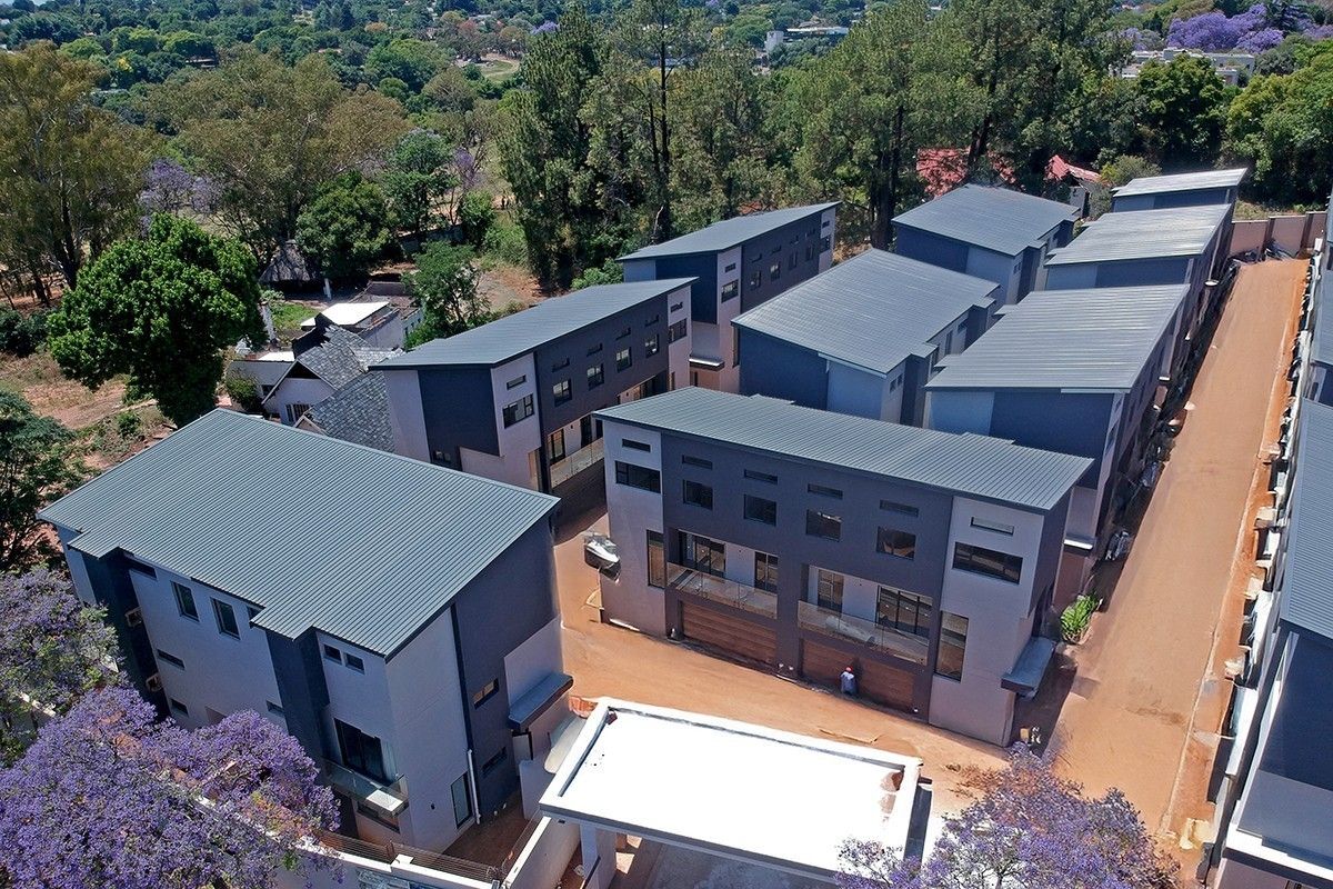 Aerial view of a modern townhouse complex featuring multiple multi-story units with metal roofing, paved driveways, and a secure entrance gate.