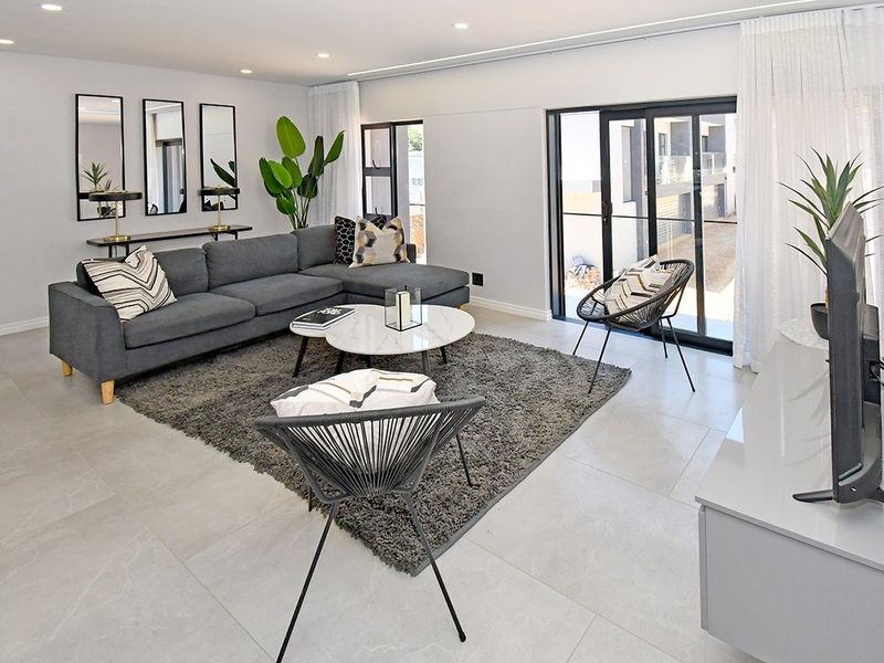 Modern, bright living room featuring large format floor tiles, recessed lighting, and sliding glass doors providing access to the exterior.