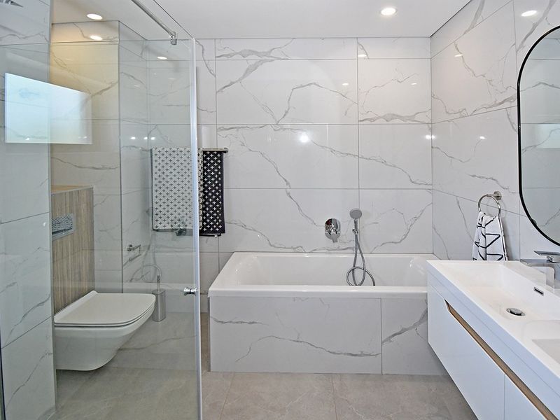 Modern bathroom featuring marble-look wall tiles, a wall-mounted toilet, a glass-enclosed shower, a built-in bathtub, and a sleek vanity with an integrated basin.
