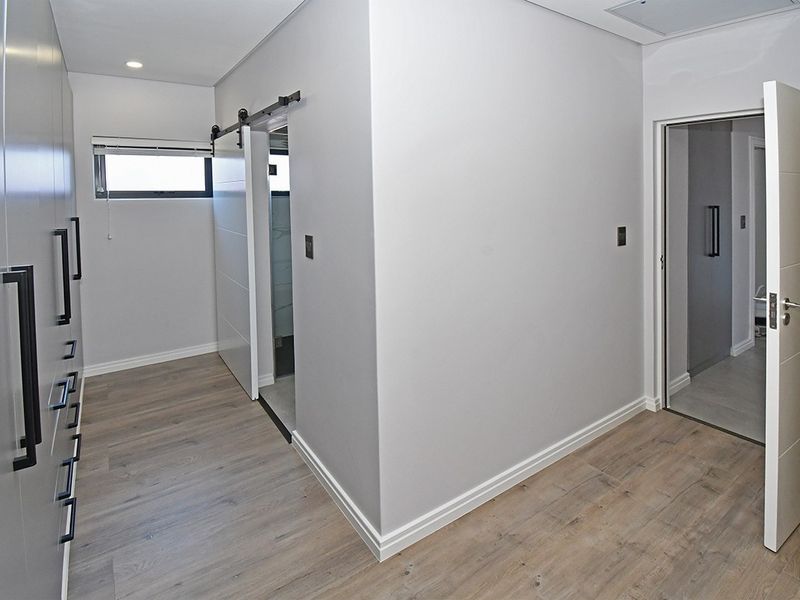 A modern, empty bedroom featuring light wood-look laminate flooring, extensive built-in cabinetry, and a sleek sliding barn door leading to an en-suite bathroom.