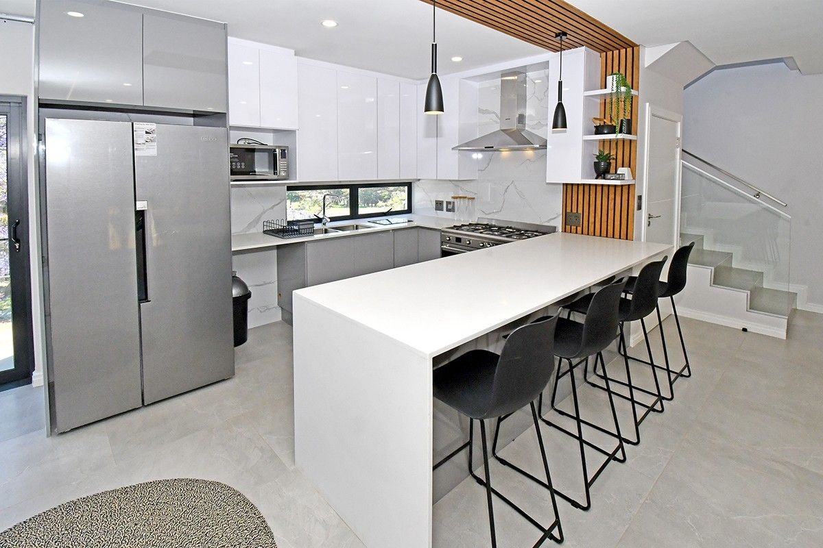 Modern kitchen featuring high-gloss cabinetry, stone countertops, a central island with breakfast bar, integrated appliances, and a stylish timber-slat feature wall.