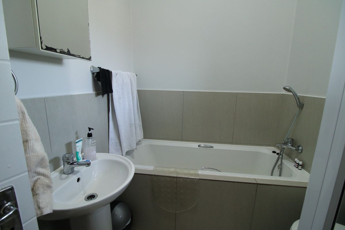 A functional bathroom featuring a pedestal washbasin, a bathtub with a handheld shower mixer, and neutral wall tiling.