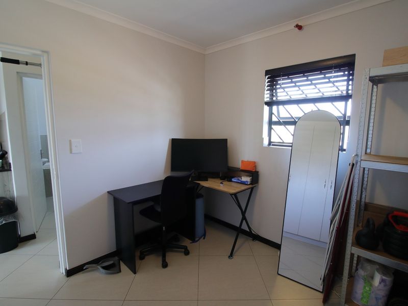 A functional office space featuring tiled flooring, a window with security bars, and venetian blinds, providing a practical area for work or study.