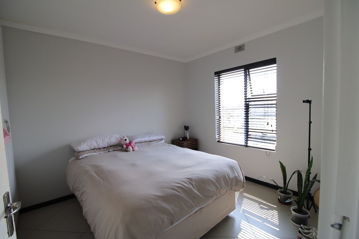 A well-lit bedroom featuring neutral walls, tiled flooring, and a window fitted with venetian blinds.