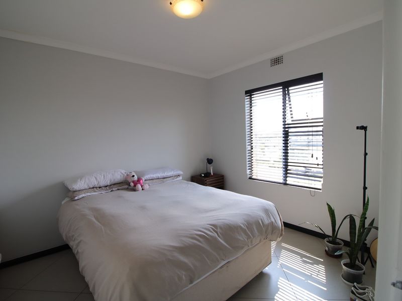 A well-lit bedroom featuring neutral walls, tiled flooring, and a window fitted with venetian blinds.