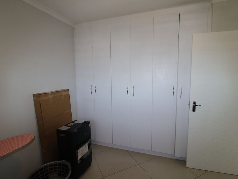 A clean, neutral bedroom featuring ample built-in cupboard storage and tiled flooring, offering a blank canvas for personalization.