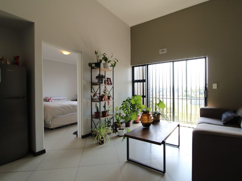 A bright living area featuring tiled floors, vaulted ceilings, and a large sliding glass door with vertical blinds leading to an outdoor space.