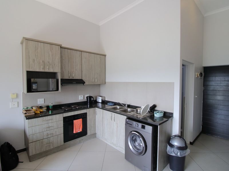 Compact modern kitchen featuring light wood-grain cabinetry, granite countertops, integrated oven, hob, extractor fan, and space for a washing machine.